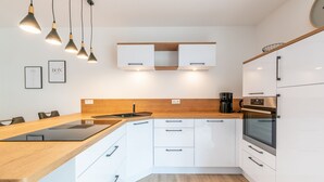 Eine moderne Küche mit weißen Schränken, einer Holz Arbeitsplatte, einem eingebauten Backofen und Pendelleuchten.