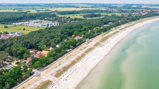 Eine Luftaufnahme einer Küstenlandschaft mit Strand, Häusern und Grünflächen.