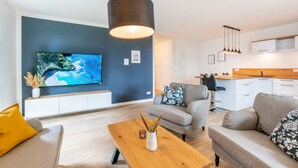Ein modernes Wohnzimmer mit einem Flachbildfernseher, einem Holztisch und einem grauen Sofa.