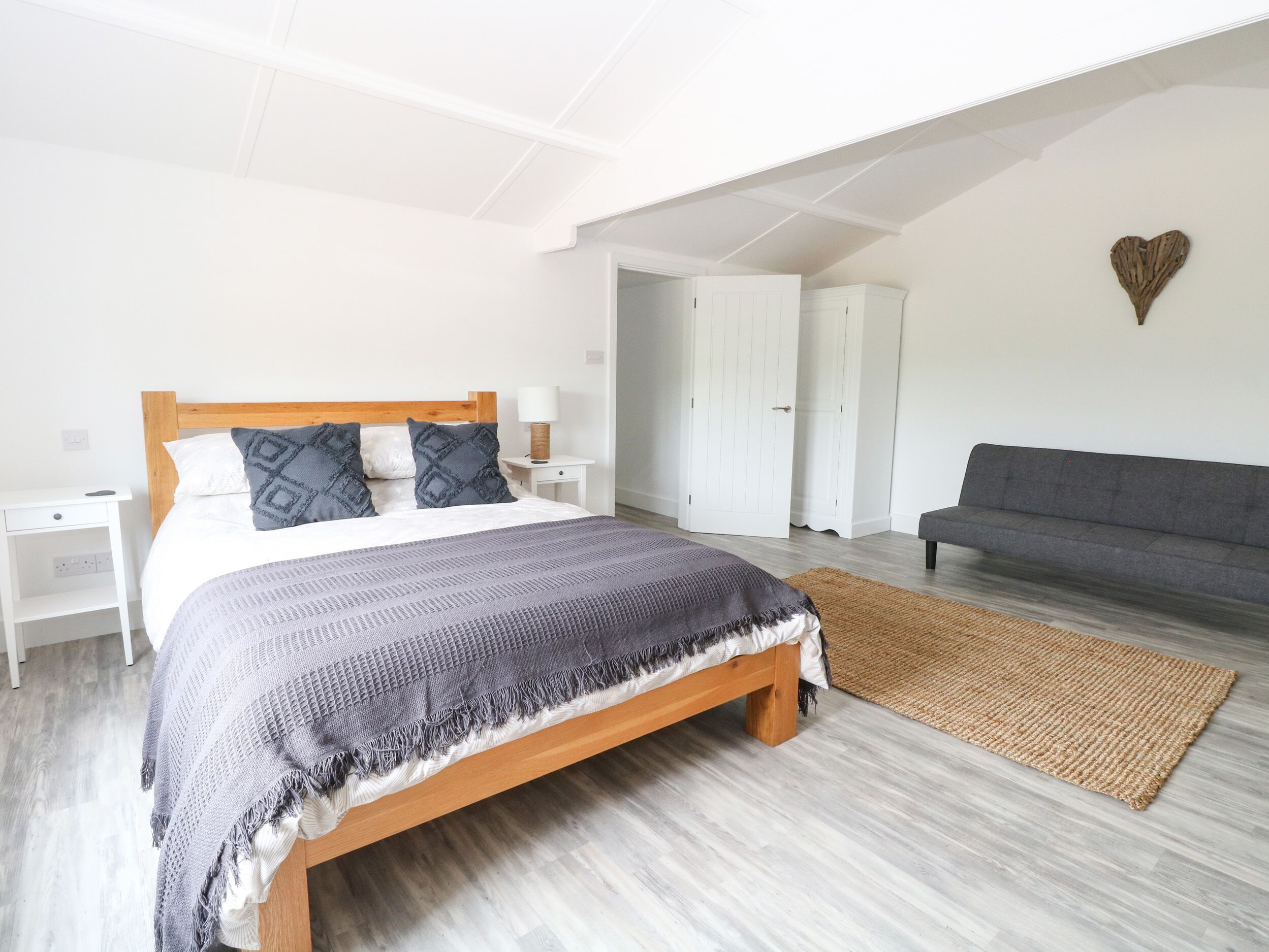 A bedroom with a wooden bed, white nightstands, a grey sofa, and a woven rug.