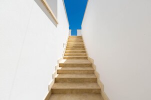 Una escalera recta color beige que sube entre paredes blancas.
