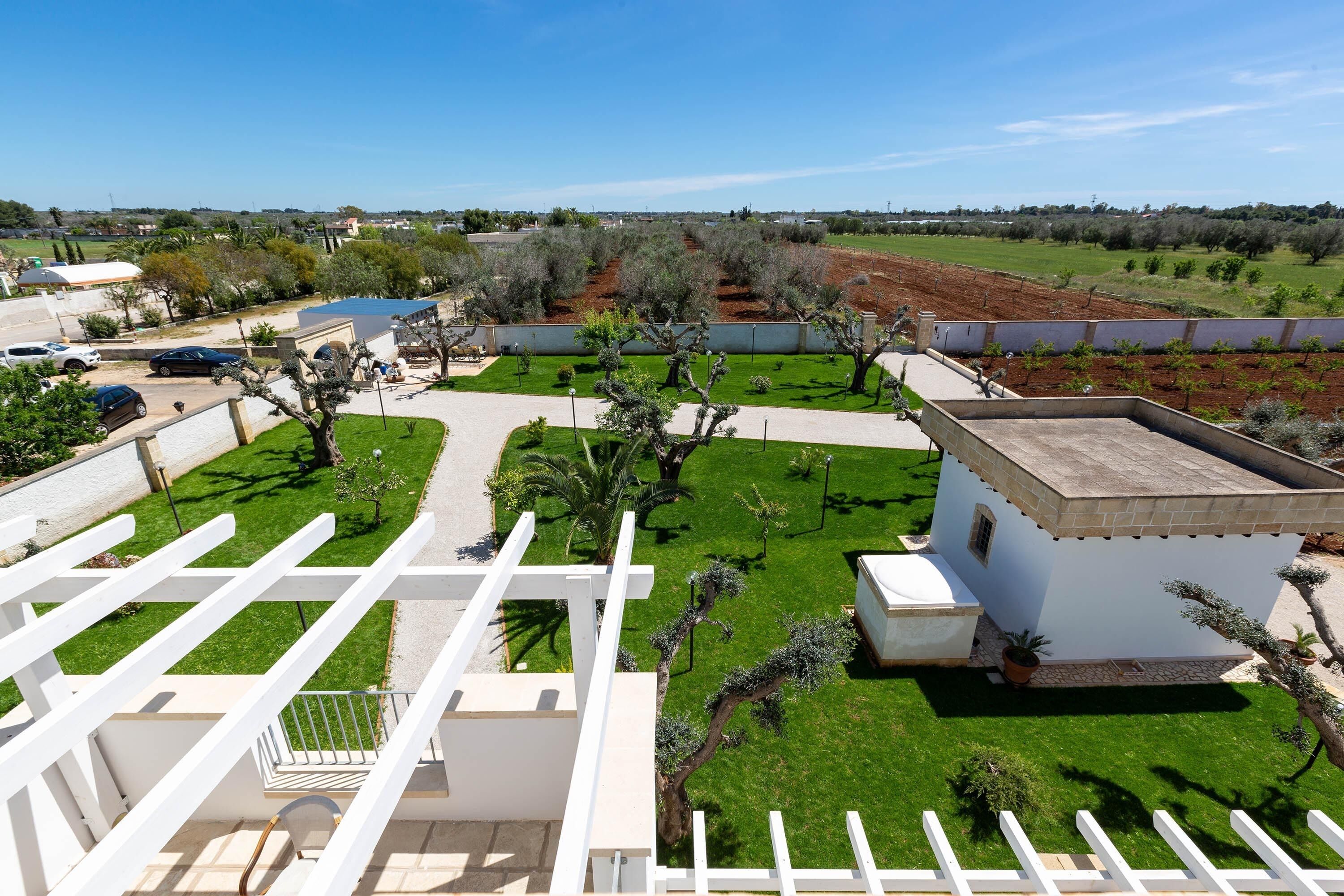 A residential area with a white building, a garden with various plants, and a clear blue sky.