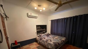 A bedroom with a bed, a ceiling fan, an air conditioner, a small table, a chair, and a window with curtains. - Stunning 2-bed House in Madina (Accra)