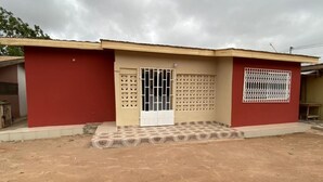 A single-story building with a red exterior, a beige door, and a barred window. - Stunning 2-bed House in Madina (Accra)