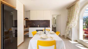 Una cocina moderna con armarios blancos, un refrigerador Bosch y un comedor con sillas amarillas y mantel blanco.