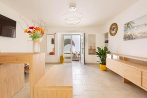 Un salón moderno con un banco de madera, una mesa de centro de cristal, un jarrón con flores, un cuadro grande y un reloj en la pared.