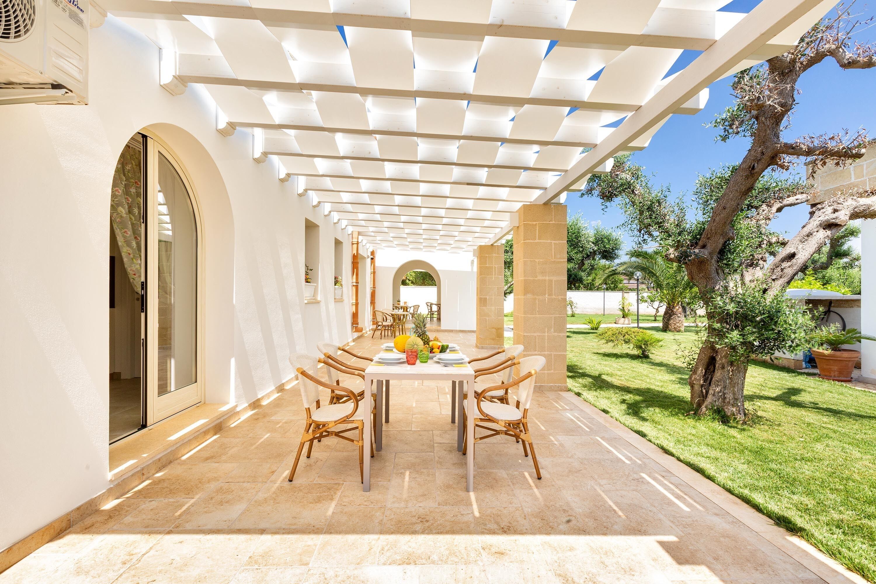 Un área de comedor al aire libre con una pérgola, una mesa con sillas y vistas al jardín.