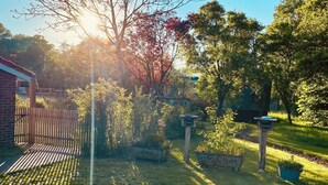 Un jardín con zona pavimentada, valla de madera y un cartel.