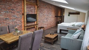 Una habitación acogedora con pared de ladrillo, una mesa de madera para comer, un sofá y una cama.