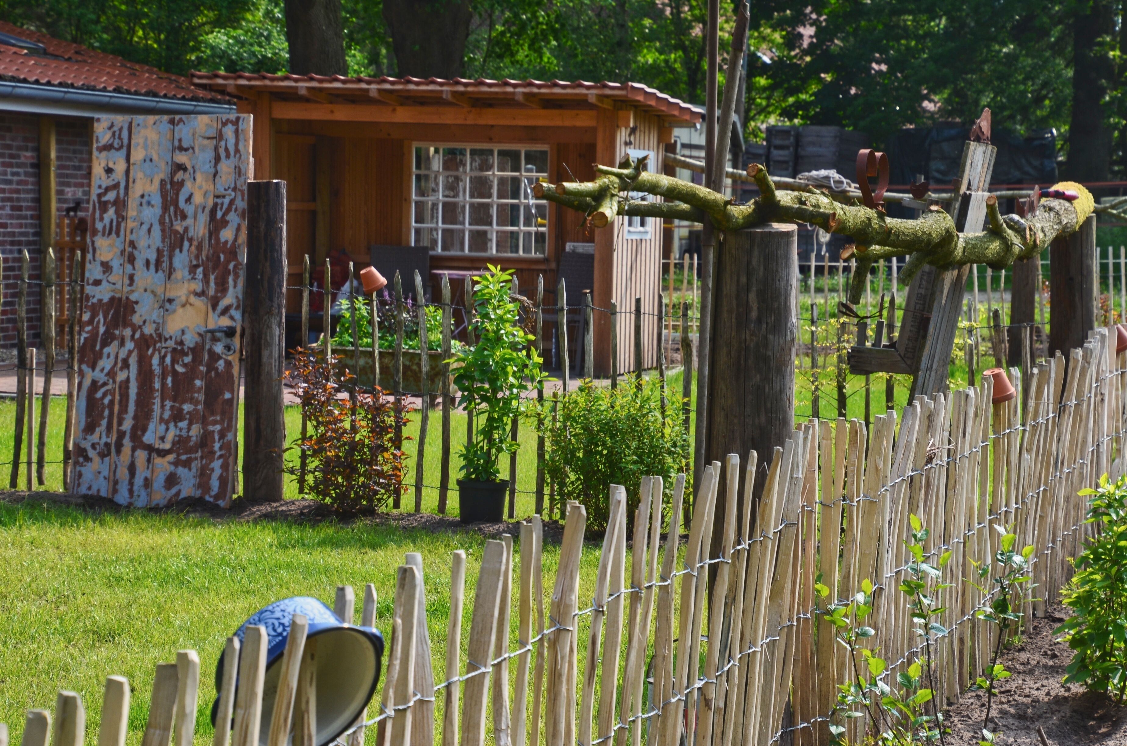 Une clôture en bois rustique surmontée de fil barbelé, un abri en bois et une petite maison avec un toit rouge.