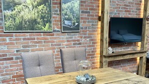 Un comedor rústico con una mesa y sillas de madera, una pared de ladrillo y un televisor montado.