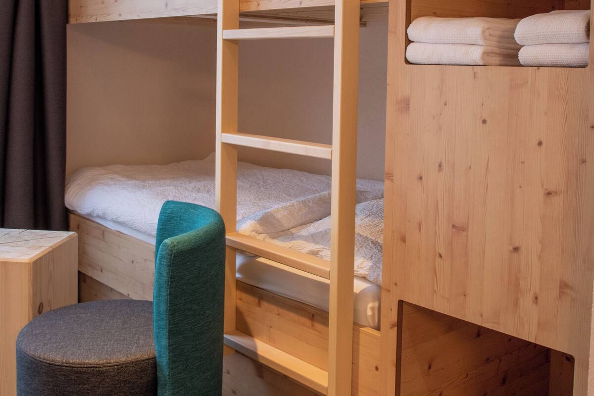 A wooden bunk bed with a pull-out desk and a cushioned stool.