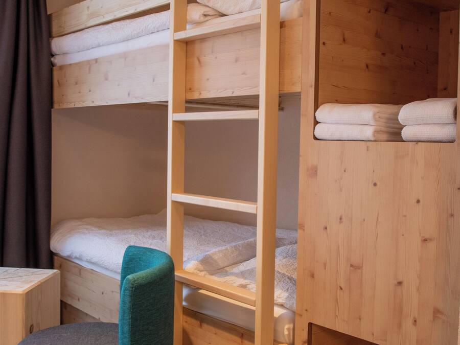 Un lit superposé en bois avec un bureau escamotable et un tabouret rembourré.