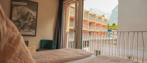 A hotel room with a large window, a bed, a chair, and a framed picture on the wall.