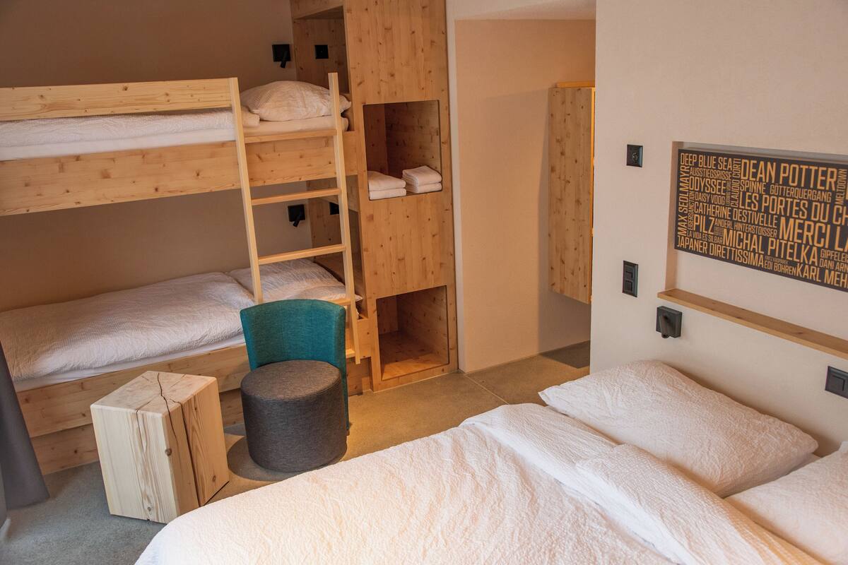 A bunk bed room with a wooden ladder, a small stool, and a wall-mounted shelf.