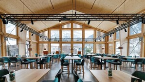 A spacious indoor area with high ceilings and large windows, featuring multiple tables and chairs arranged for dining or meetings. - Eiger Lodge Chic (Grindelwald)