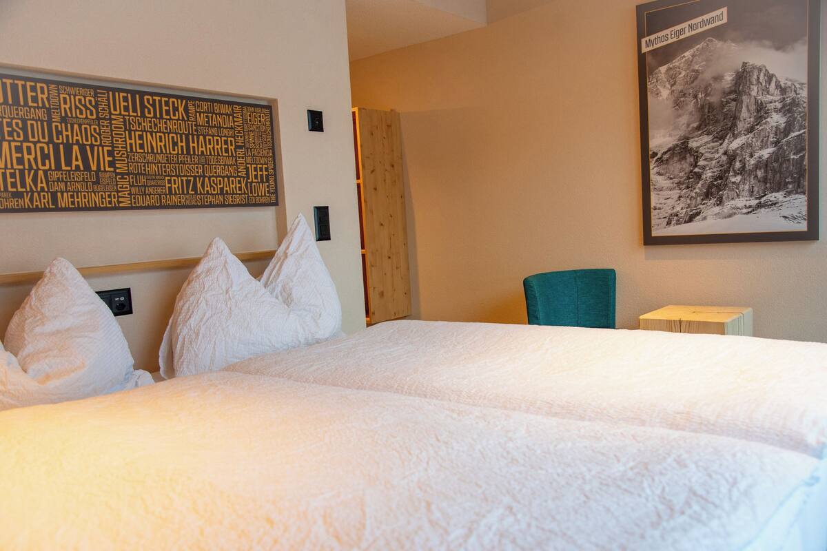 A hotel room with a large bed, pillows, a wooden headboard, a framed picture on the wall, and a small table with a lamp.