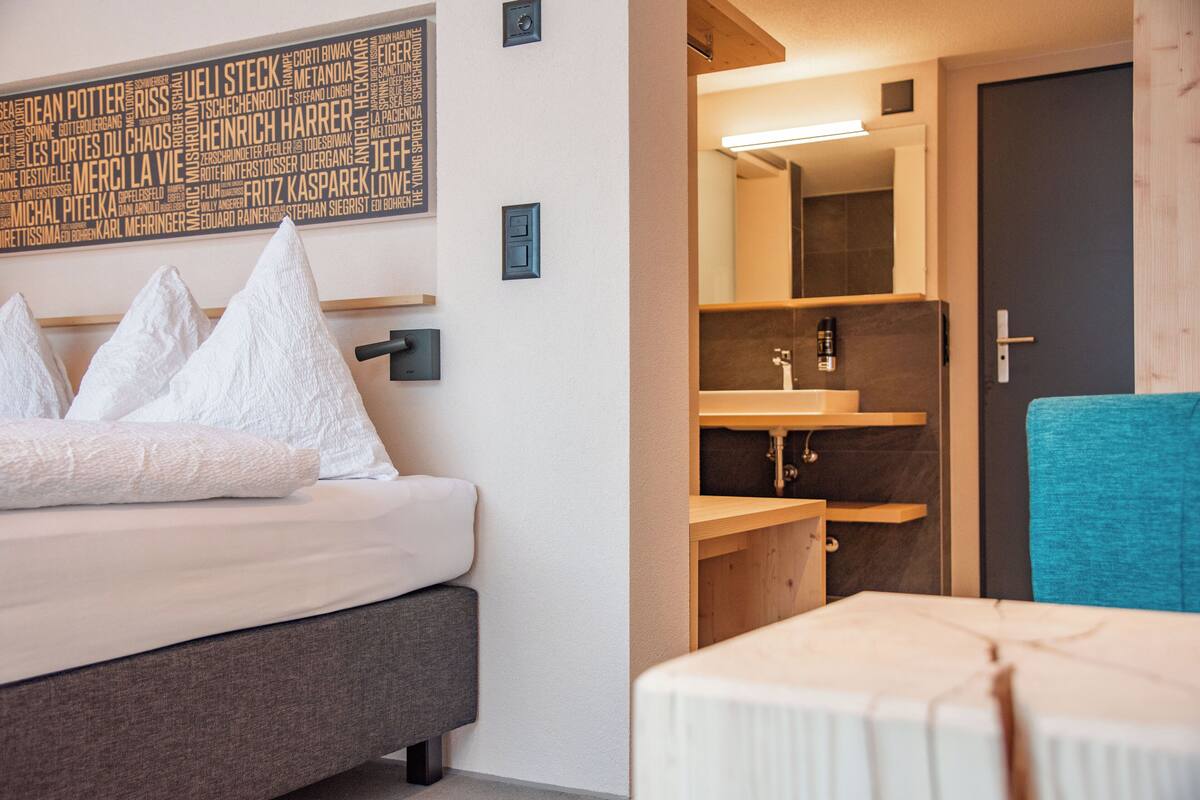 A hotel room with a bed, a bedside table, a bathroom with a mirror, sink, and towel rack.
