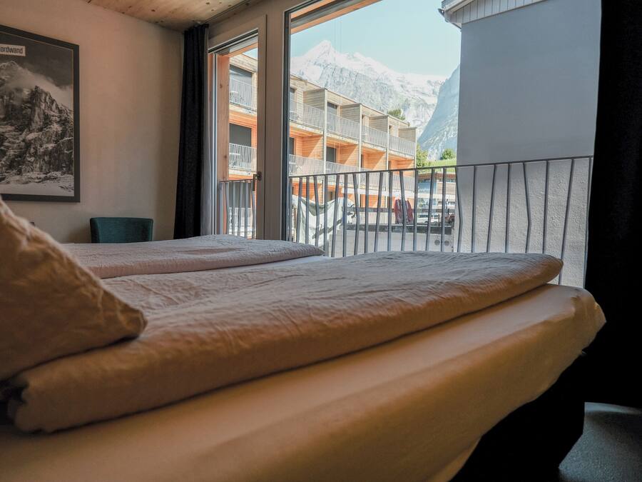 Ein Hotelzimmer mit Bett, Fenster mit Bergblick und einem gerahmten Bild an der Wand.