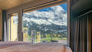 A room with a large window offering a view of snow-covered mountains and a village below. - Eiger Lodge Chic (Grindelwald)