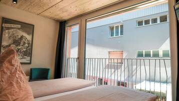 A bedroom with two beds, a framed picture on the wall, a green chair, and a balcony with a railing.