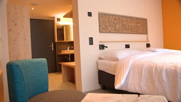 Una habitación de hotel con una cama, una silla, un escritorio con espejo y una obra de arte en la pared.