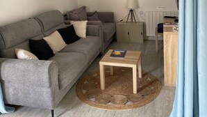 Een woonkamer met een grijze bank, een klein houten tafeltje, een lamp en een radiator.