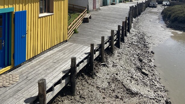 Een houten looppad leidt naar kleurrijke strandhutten met betegelde daken.