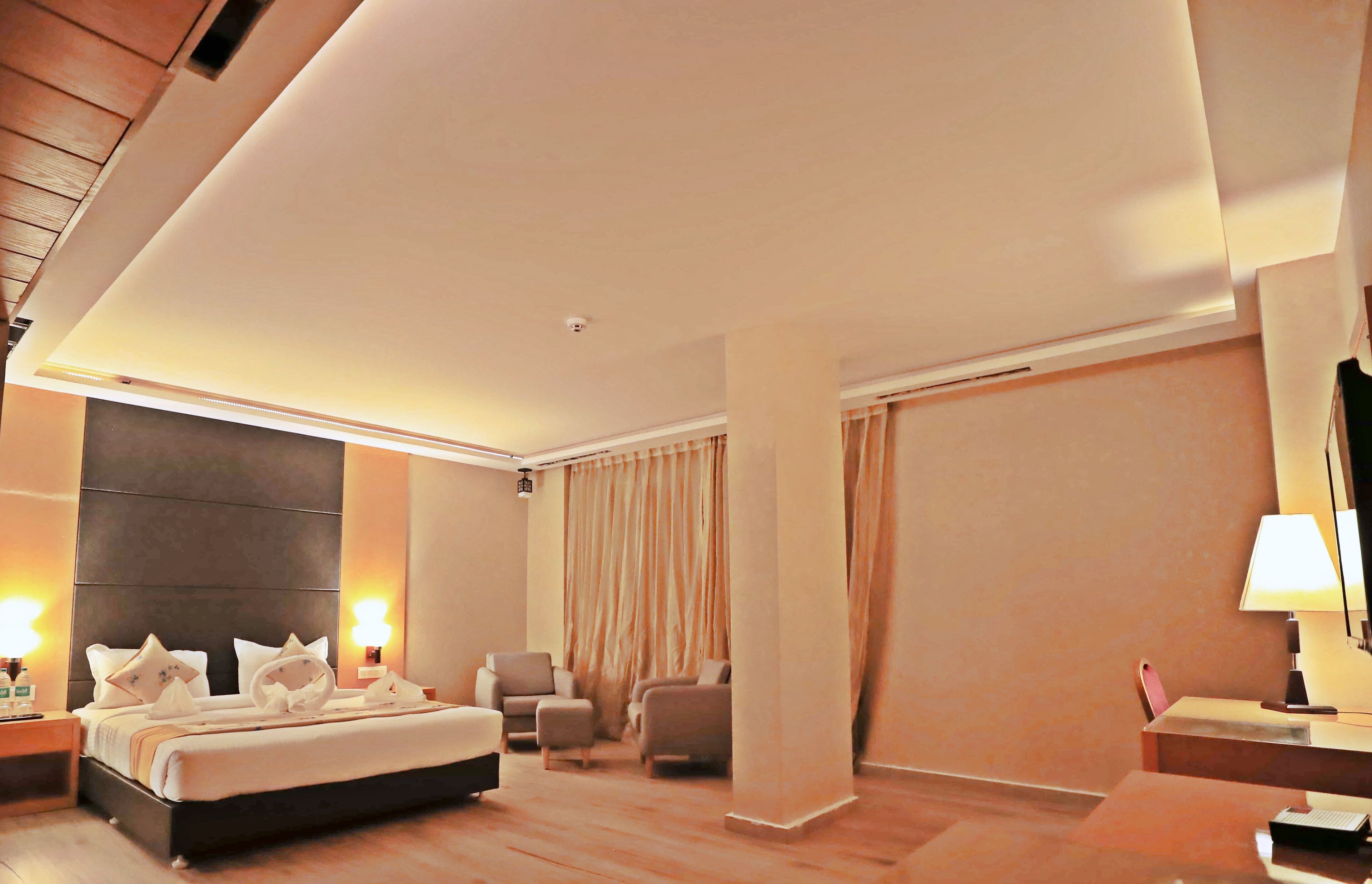 Una habitación de hotel moderna con una cama grande, dos sillones, un escritorio y un ventanal con cortinas.