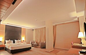 Une chambre d’hôtel moderne, dotée d’un grand lit, de deux fauteuils, d’un bureau et d’une grande fenêtre avec des rideaux.