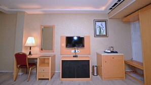 Habitación de hotel con escritorio, silla, televisión y un pequeño armario.
