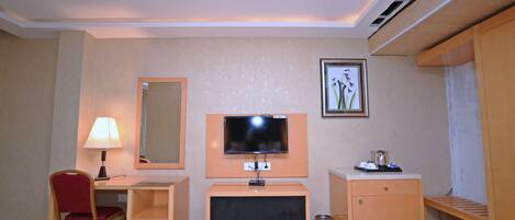 A hotel room with a desk, chair, TV, and a small cabinet.