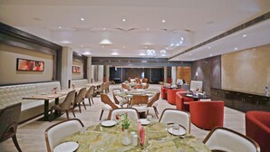 Un comedor amplio con varias mesas y sillas, un área de estar central con un sofá, y una pared grande con obras de arte.