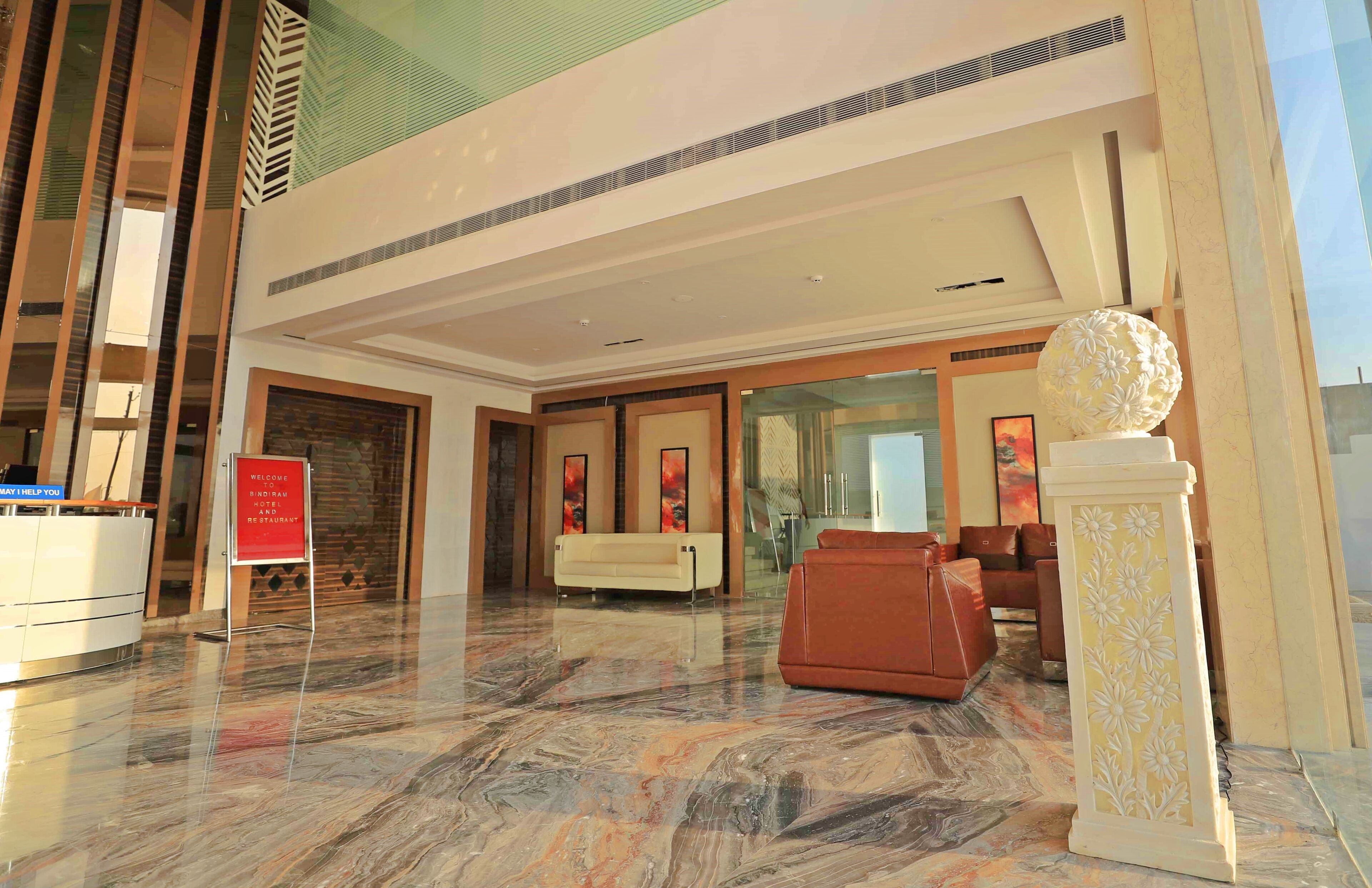 A modern hotel lobby with a reception desk, seating area, and a decorative column.