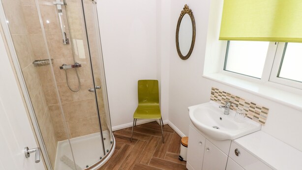 A bathroom with a glass shower enclosure, a green chair, a white sink, and a mirror above the sink. - 1 The Warren (Narberth)