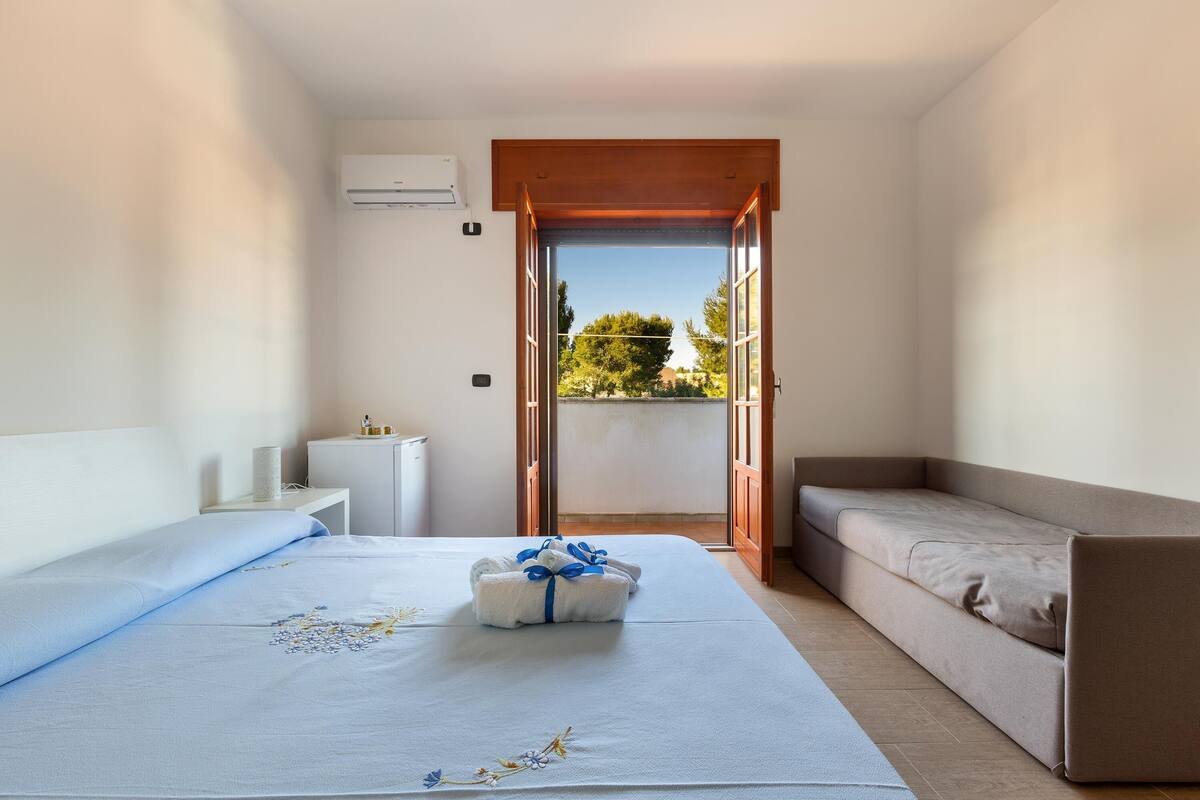 A bedroom with a bed, a sofa, a small table, and an air conditioning unit.
