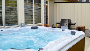 A hot tub with a stone wall and a grill in the background. - Spacious 3-bedroom home with ski in/out access to Orient Chair and private hot tub! (Sun Peaks)