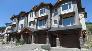 A multi-story residential building with stone pillars, multiple garage doors, and a clear driveway. - Spacious 3-bedroom home with ski in/out access to Orient Chair and private hot tub! (Sun Peaks)
