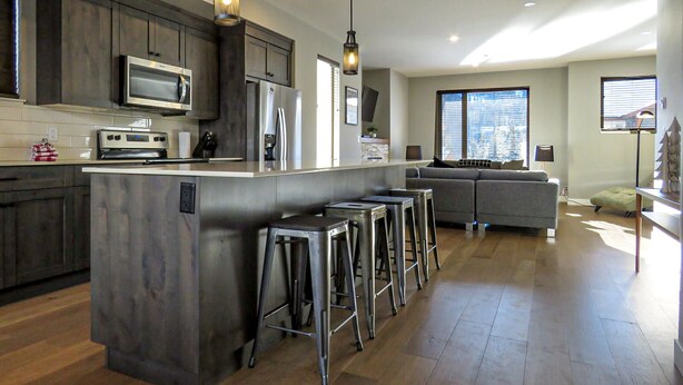 A modern kitchen with dark wood cabinets, stainless steel appliances, and a central island with stools. - Spacious 3-bedroom home with ski in/out access to Orient Chair and private hot tub! (Sun Peaks)
