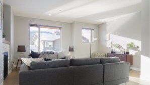 A modern living room with a grey sectional sofa, a small side table, and a floor lamp. - Spacious 3-bedroom home with ski in/out access to Orient Chair and private hot tub! (Sun Peaks)