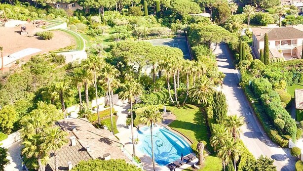 A resort with a swimming pool surrounded by palm trees and a view of the sea.