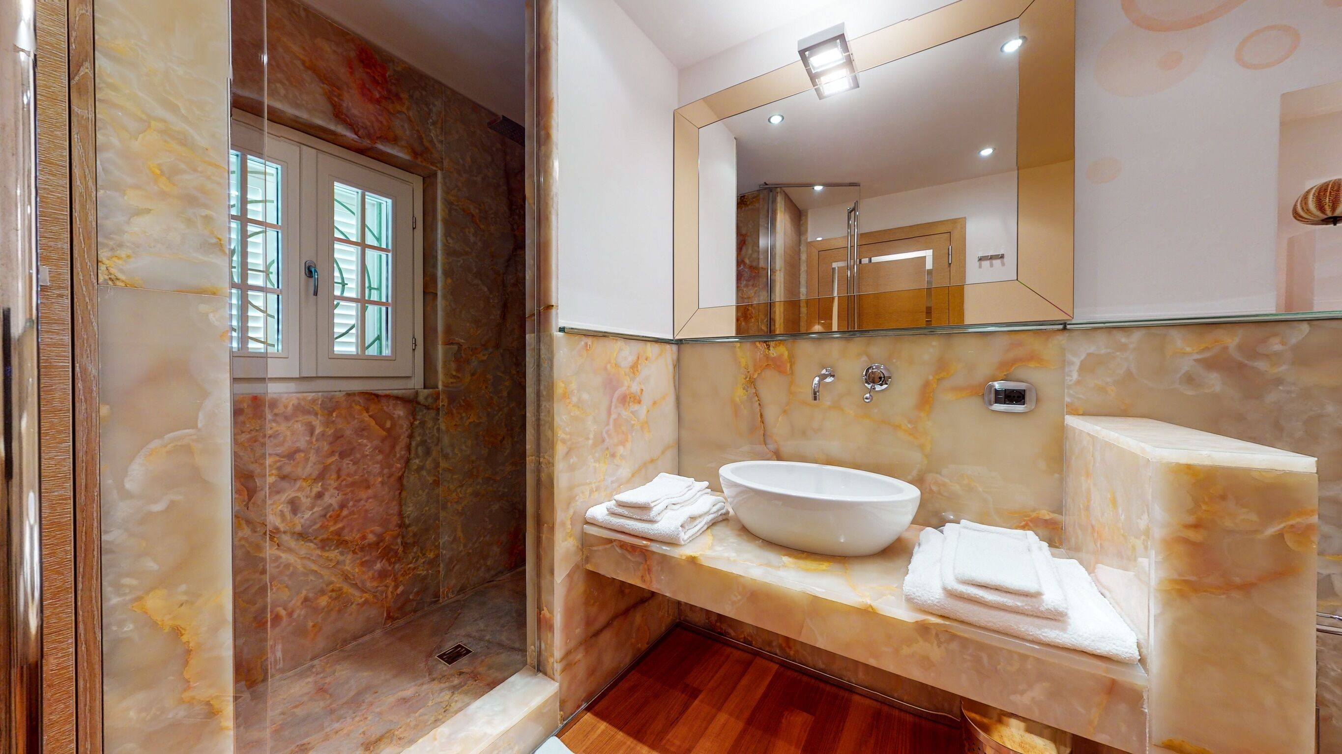 A bathroom with a marble vanity, a large mirror, and a glass-enclosed shower area.