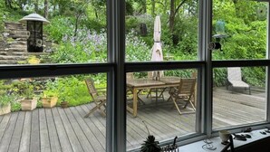 A conservatory with a view of a wooden deck, outdoor furniture, and lush greenery. - Peacock Garden Cottage - Discounted for Winter Month Rental (Pine plains)
