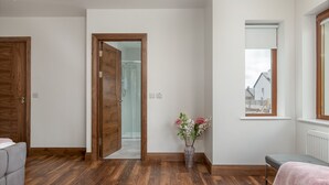 Ein modernes Zimmer mit Holzboden, einer Duschkabine aus Glas, einer Vase mit Blumen und Blick auf ein Gebäude durch ein Fenster.