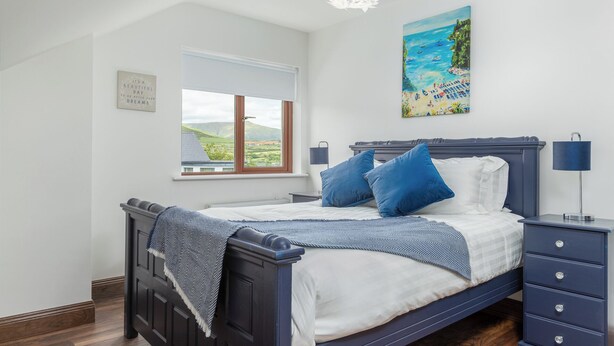Ein Schlafzimmer mit Bett, Nachttisch, Kommode, einem Fenster mit Blick auf die Landschaft und einem Bild an der Wand.