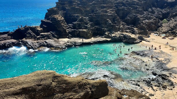 Un paysage côtier caractérisé par des falaises rocheuses, des eaux turquoise et limpides, et une plage de sable.