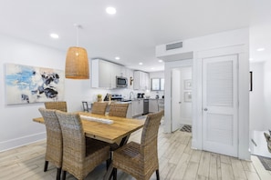A modern kitchen with white cabinets, a dining table with wicker chairs, and a hanging pendant light.