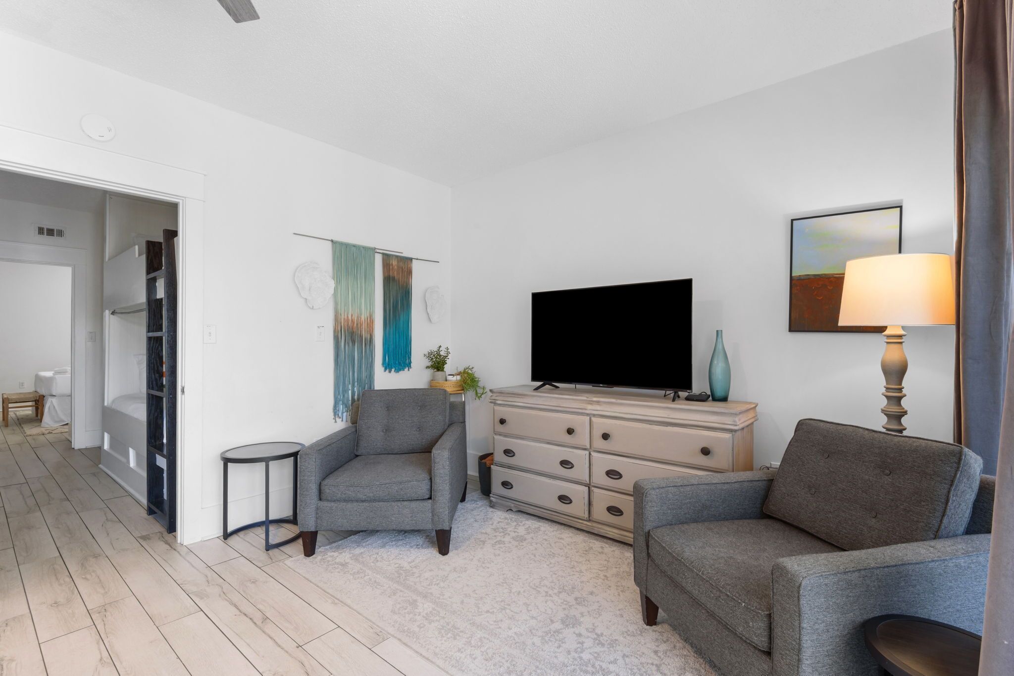 A modern living room with a flat-screen TV, two grey sofas, a small side table, a cabinet with drawers, and a painting on the wall.