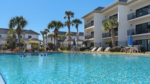 A swimming pool with lounge chairs and umbrellas, surrounded by palm trees and a multi-story building. - Remodeled Seagrove Condo ~ Pool ~ Steps to Beach + Free Attraction Tickets! (Santa Rosa Beach)
