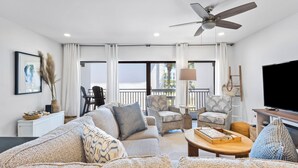 A modern living room with a sofa, armchairs, a coffee table, a TV, and a ceiling fan. - Remodeled Seagrove Condo ~ Pool ~ Steps to Beach + Free Attraction Tickets! (Santa Rosa Beach)